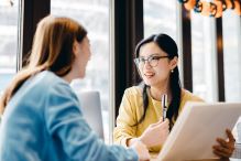 Two women engaged in conversation while seated at a table.