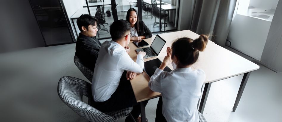 A group of professionals with laptops collaborates around a table, discussing strategies for top recruitment agencies in China.