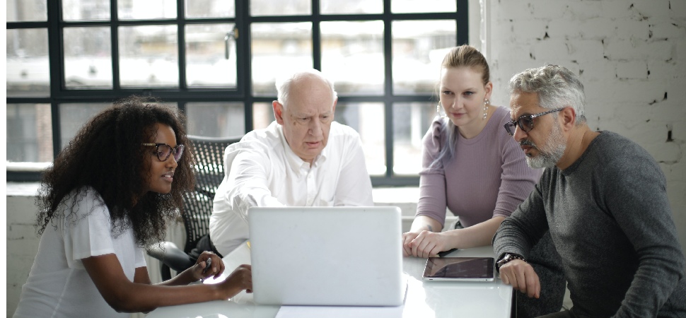 A group of four professionals of different age groups seated and looking at a laptop screen, illustrating an age-inclusive work environment