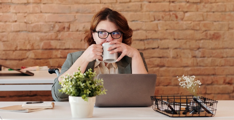 Female office worker in a wheelchair drinking from a mug while sitting at a work desk with a laptop