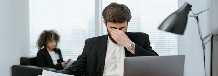 A frustrated man in a suit sits at a desk with a laptop, engaged in a tense salary increment discussion.