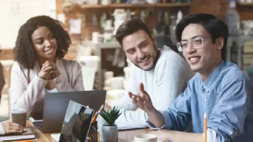 A diverse group of white-collar professionals sitting around a table, smiling, and having a discussion.