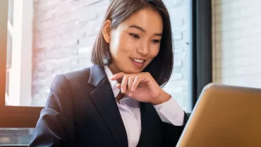 East Asian woman in her 30s smiling and looking at her laptop screen