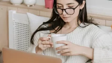 woman sitting on her bed looking at a computer screen