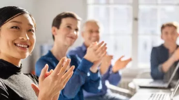 A group of office workers clapping and sitting at a long conference table