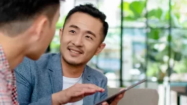 A male professional holding a tablet and in discussion with another male professional