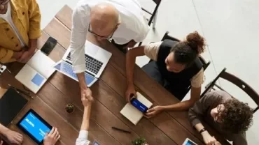 A group of professionals engaged in leadership networking, sitting around a table with laptops and tablets