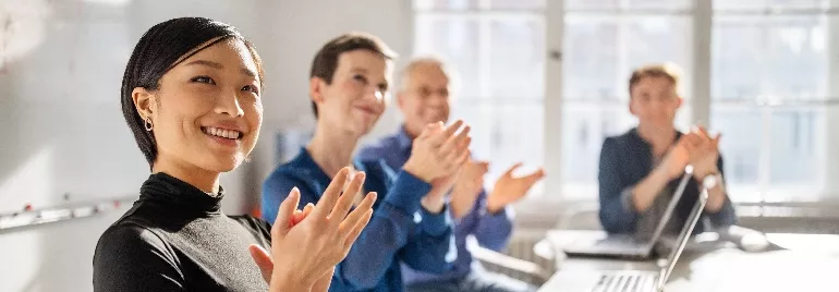 A group of office workers clapping and sitting at a long conference table