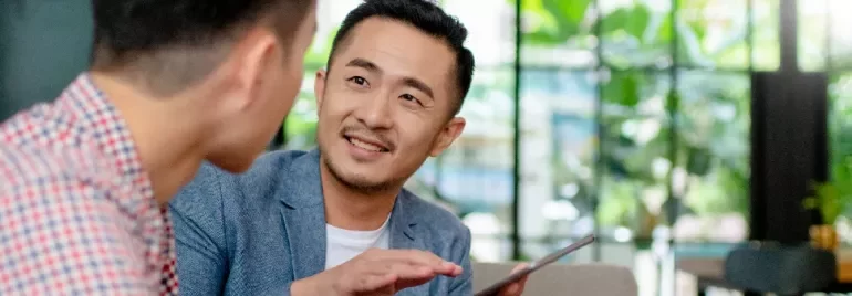 A male professional holding a tablet and in discussion with another male professional