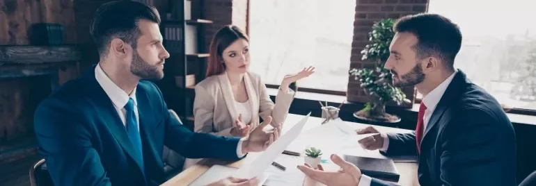 Three business professionals engaged in discussion while seated at a table