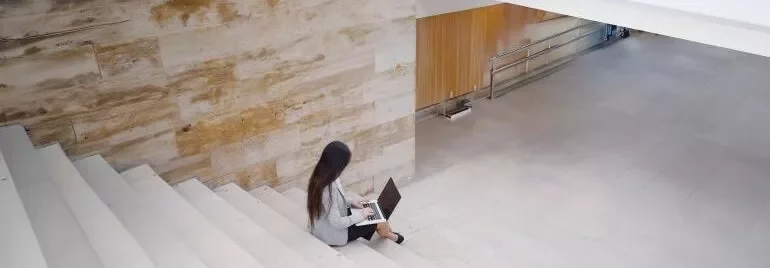 A woman using her laptop while sitting on a staircase, appearing engaged in her work.