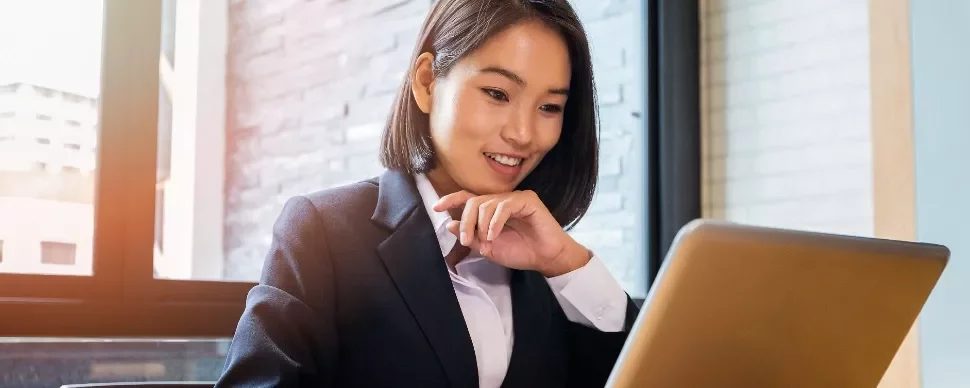 East Asian woman in her 30s smiling and looking at her laptop screen