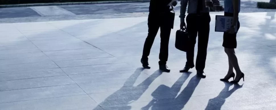 Three business professionals standing together in front of a modern office building, engaged in conversation.
