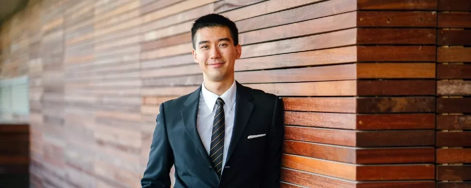 Asian man in a business suit standing against a wall