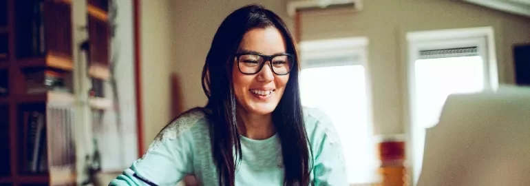 East Asian female professional smiling as she works on the laptop.
